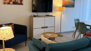 Ein modernes Wohnzimmer mit einer Couch, einem Fernseher, einer Lampe und einem Gemälde an der Wand.
