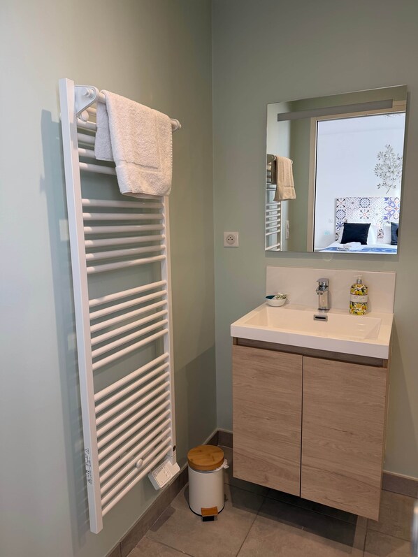 A bathroom with a white towel rack, a sink with a mirror above it, and a small trash bin.