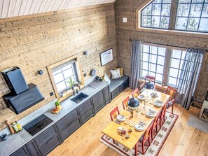 A modern kitchen with a long countertop, a dining area with a wooden table and red chairs, and large windows with a view of trees.