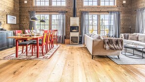 Una habitación amplia con techo alto, paredes de madera, chimenea, zona de comedor con sillas rojas y un sofá.