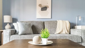 Una sala de estar moderna con un sofá gris, una mesita auxiliar blanca, una lámpara y una pequeña planta en maceta sobre una bandeja.