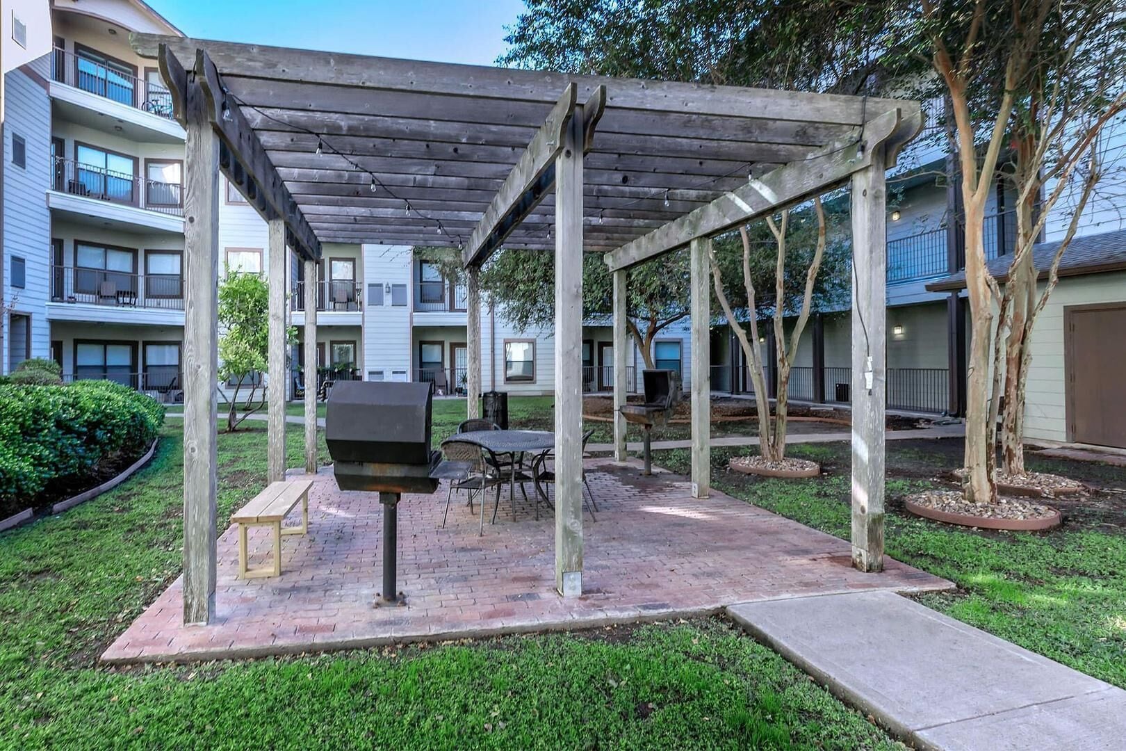 A covered outdoor area with a grill, seating, and a view of apartment buildings.