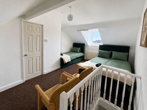 A bedroom with a sloped ceiling, a window, a bed, a chair, and a crib. - Stay for 12 | Families/Contractors | Near Doncaster Station+City Centre |Parking (Doncaster)