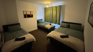 Een hotelkamer met twee eenpersoonsbedden, een tafeltje, een stoel, een raam met gordijnen en een plafondlamp.
