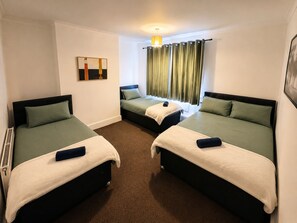 Habitación de hotel con dos camas, ventana con cortinas, un cuadro en la pared y una lámpara en el techo.