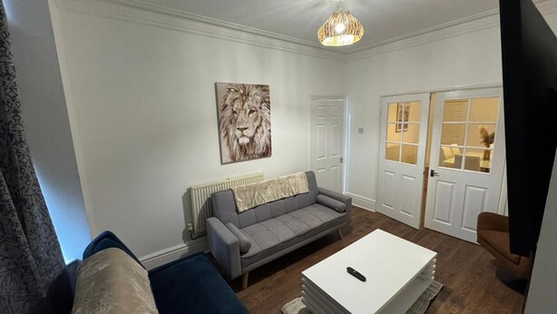 Een woonkamer met een grijze bank, een witte salontafel en een schilderij van een leeuw aan de muur.