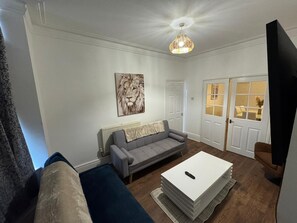 A living room with a grey sofa, a white coffee table, and a painting of a lion on the wall.