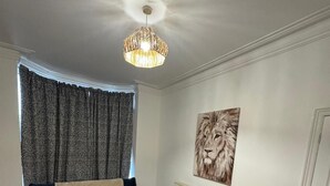 Een woonkamer met een hoekbank, een witte salontafel, een plafondlamp en een schilderij van een leeuw aan de muur.