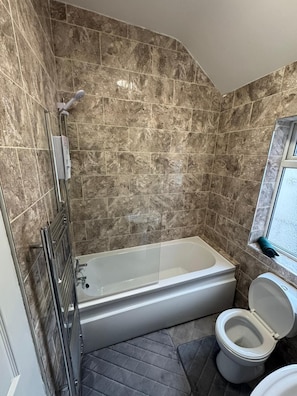 A bathroom with a bathtub, toilet, and a window.