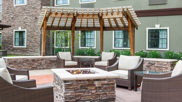 An outdoor patio area with wicker furniture, a stone fire pit, and a pergola. - Studio Suite in Houston's Energy Corridor | Free Breakfast + 24h Business Center (Houston)