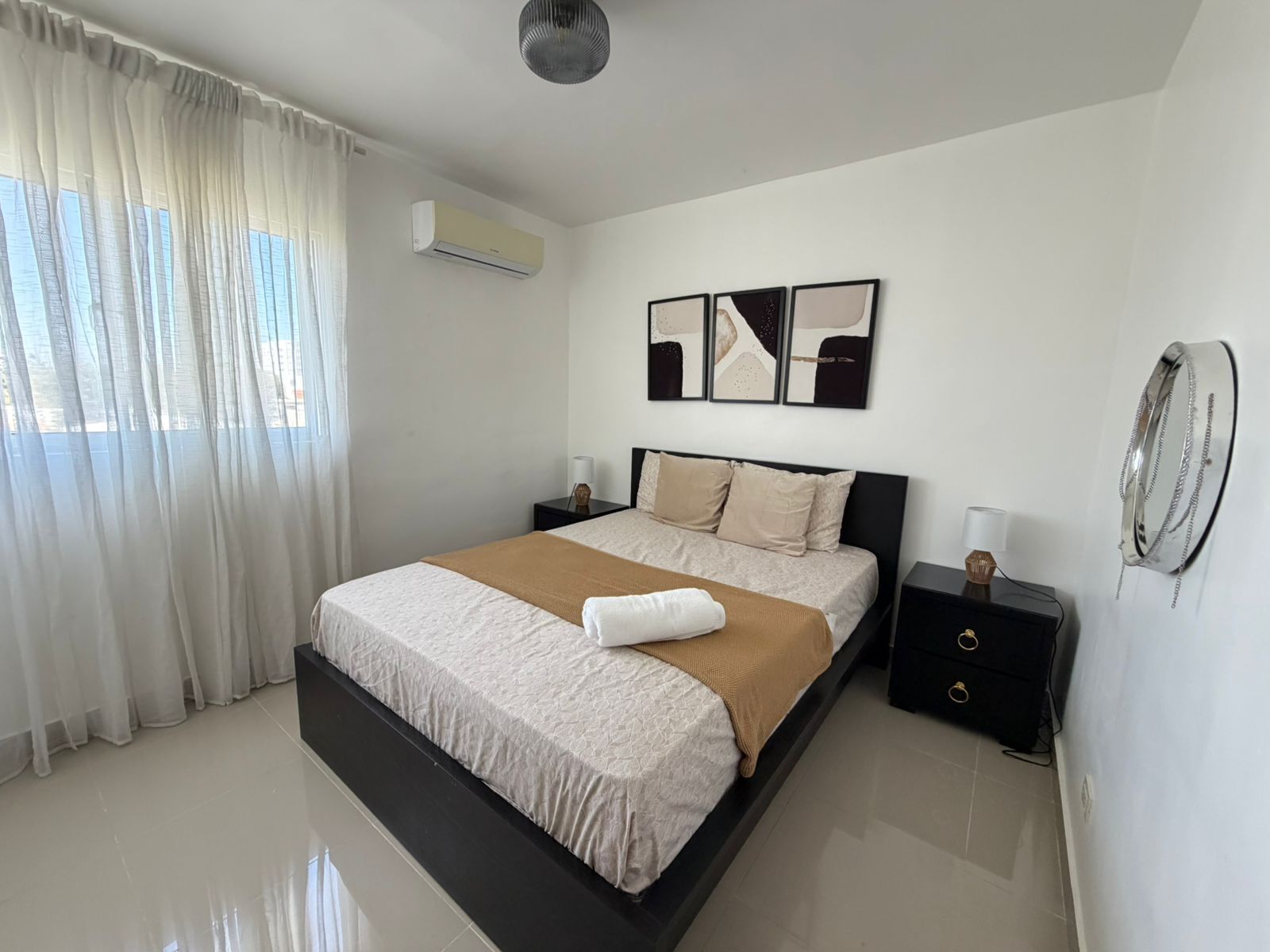 Un dormitorio moderno con una cama grande, cortinas blancas, un equipo de aire acondicionado y arte abstracto en la pared.