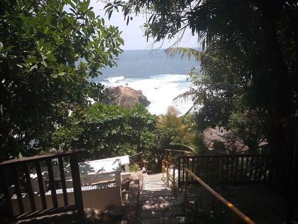 A staircase leading to a beach with ocean views, surrounded by trees and a wooden railing.