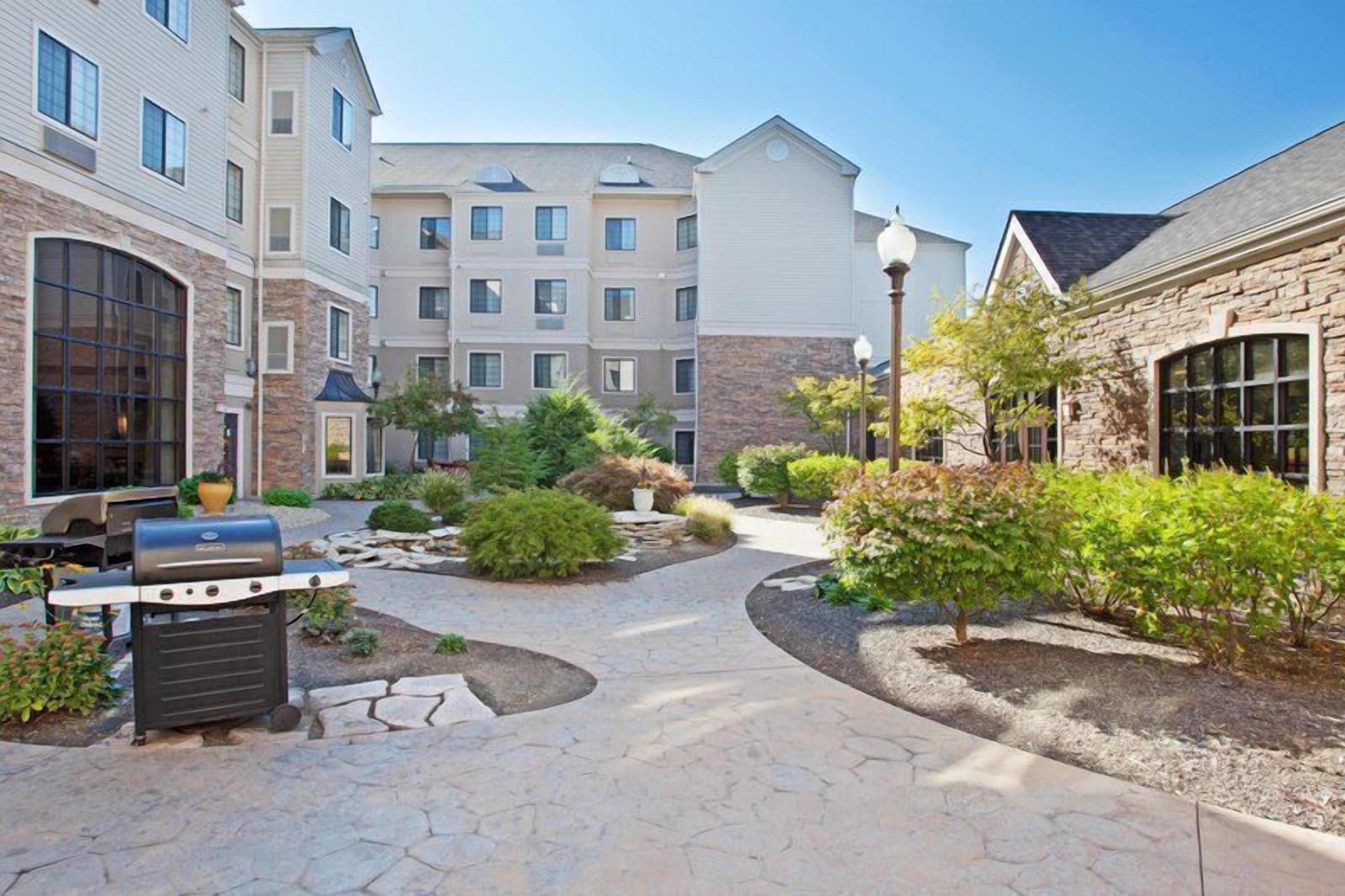 A courtyard with a barbecue grill, stone pathways, and a building with multiple windows and balconies.