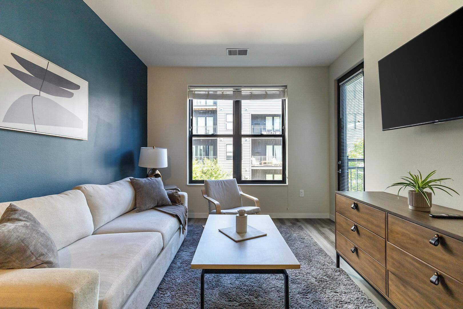 A modern living room with a sofa, a coffee table, a lamp, a TV, and a window with blinds.