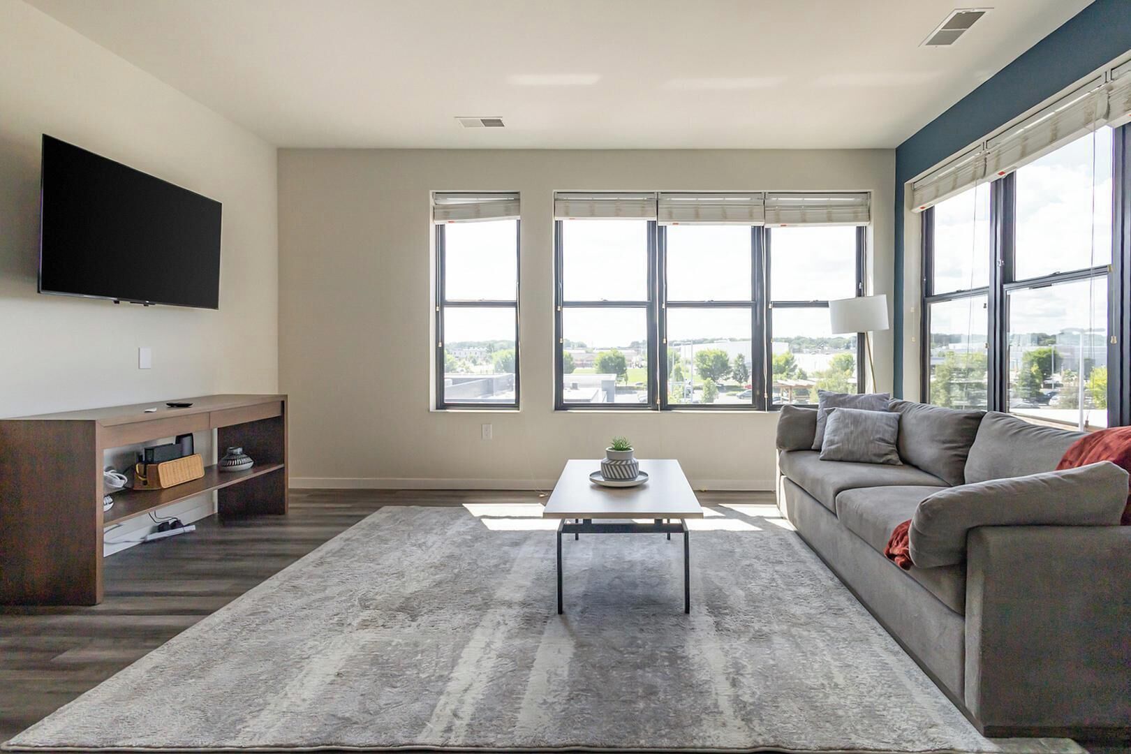 Una sala moderna con una televisión de pantalla plana, un sofá, una mesa de centro y un ventanal con vistas a la ciudad.