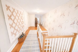 A hallway with patterned wallpaper, a wooden floor, and a staircase with a wooden railing. - New Hampshire Room: luxurious king size bed & private bath in historic B&B (Enfield)