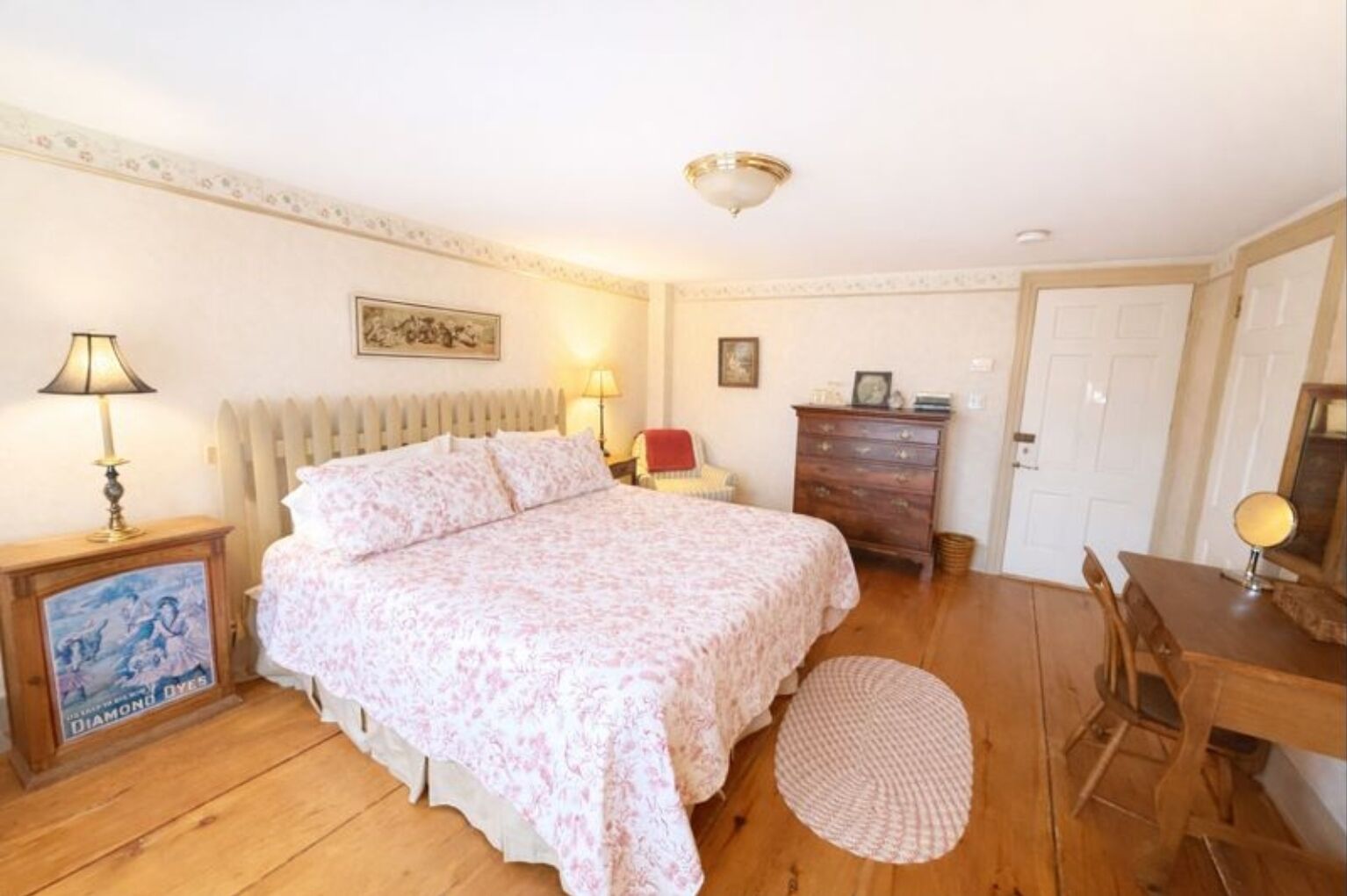 A bedroom with a bed, bedside lamps, a dresser, a chair, a round rug, and a door.