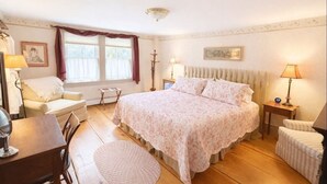 A bedroom with a large bed, a chair, a small table, and a lamp.