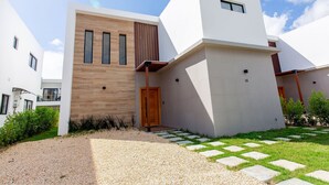A modern building with a wooden facade, a gravel driveway, and a garden with stepping stones. - Three-bedroom villa with private pool (Punta Cana)