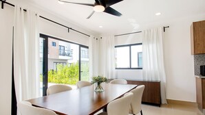 A modern dining area with a wooden table and six chairs, large windows with curtains, and a ceiling fan. - Three-bedroom villa with private pool (Punta Cana)