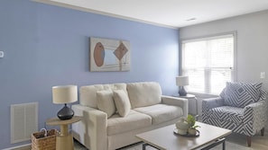 A living room with a light blue wall, a beige sofa, a patterned armchair, a coffee table, and a floor lamp.
