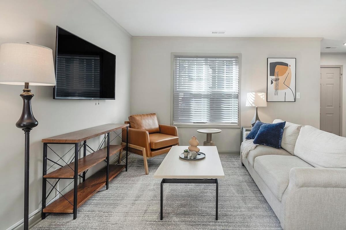 Una sala de estar moderna con un sofá, un sillón, una mesa de centro y un televisor montado en la pared.