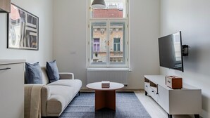 Ett modernt vardagsrum med en soffa, ett soffbord, en tv och ett fönster med utsikt över byggnader.