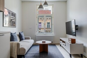 Ein modernes Wohnzimmer mit Sofa, Couchtisch, Fernseher und einem Fenster mit Blick auf Gebäude.