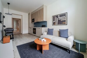 Ein modernes Wohnzimmer mit einer Couch, einem Couchtisch und einer Küchenzeile mit Schränken und Geräten.