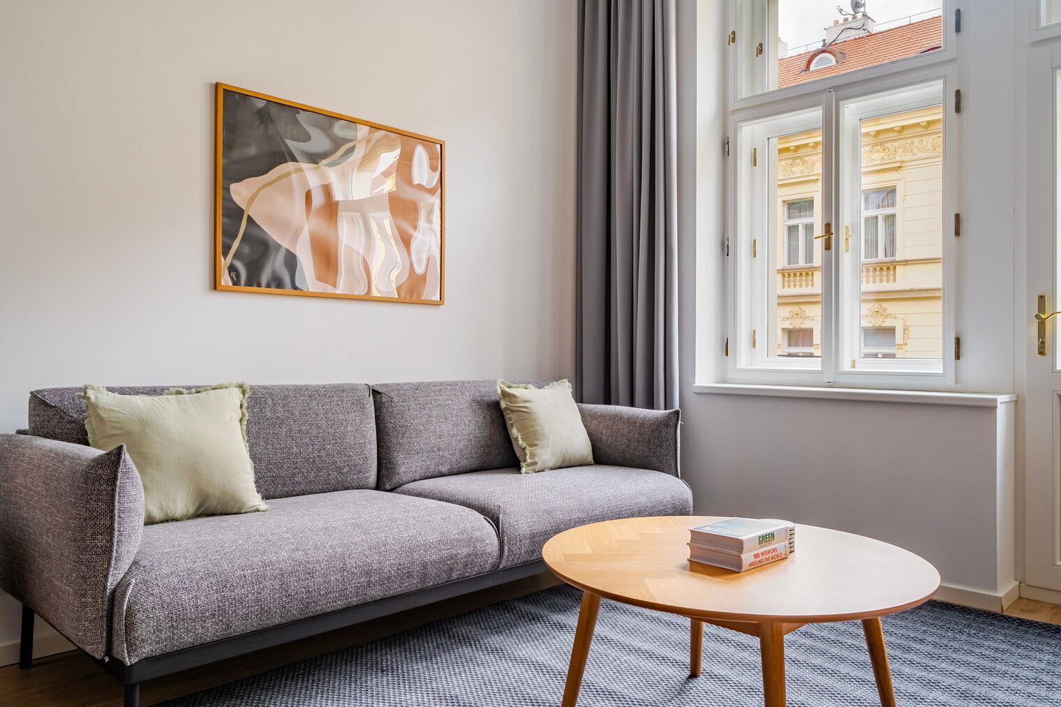 Un salon moderne avec un canapé gris, une table basse ronde en bois et une grande fenêtre avec des rideaux.