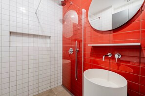 A modern bathroom with white and red tiles, a large mirror, a white sink, and a shower area. - Blueground | Vinohrady, balcony, nr Riegrovy Sady (PRG-78) (Prague)