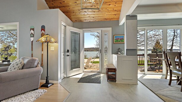 A spacious living room with a wooden ceiling, a sofa, a floor lamp, and a view of a lake through glass doors.