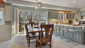 A modern kitchen with a dining area, large windows, and a view of the outdoors.