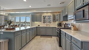 A modern kitchen with grey cabinets, a large island, stainless steel appliances, and a view of the outdoors.