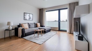 A modern living room with a grey sectional sofa, a small round coffee table, a floor lamp, and a flat-screen TV. - Blueground | Invalidovna, balcony, nr Vltava (PRG-90) (Prague)