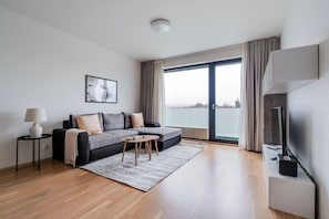 A modern living room with a grey sectional sofa, a small round coffee table, a floor lamp, and a flat-screen TV. - Blueground | Invalidovna, balcony, nr Vltava (PRG-90) (Prague)