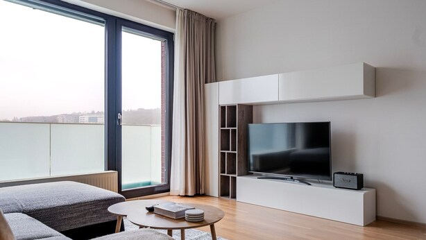 A modern living room with a large TV, a sofa, a coffee table, and a balcony with a view. - Blueground | Invalidovna, balcony, nr Vltava (PRG-90) (Prague)