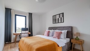 A hotel room with a bed, a desk, a chair, a nightstand, and a window with curtains. - Blueground | Invalidovna, balcony, nr Vltava (PRG-90) (Prague)