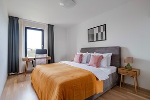 A hotel room with a bed, a desk, a chair, a nightstand, and a window with curtains. - Blueground | Invalidovna, balcony, nr Vltava (PRG-90) (Prague)