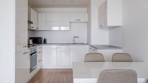 A modern kitchen with white cabinetry, a built-in oven, a microwave, and a sink. There is a dining table with two chairs. - Blueground | Invalidovna, balcony, nr Vltava (PRG-90) (Prague)