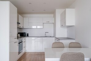 A modern kitchen with white cabinetry, a built-in oven, a microwave, and a sink. There is a dining table with two chairs. - Blueground | Invalidovna, balcony, nr Vltava (PRG-90) (Prague)