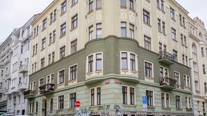 Un edificio de varios pisos con fachada verde en una esquina, varios balcones y un letrero de no estacionamiento.