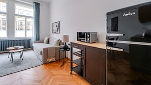 Un espacio habitable compacto con kitchenette, un sofá, una mesita y una ventana con cortinas.