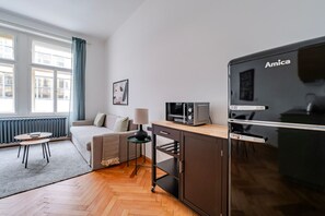 A compact living space with a kitchenette, a sofa, a small table, and a window with curtains. - Blueground | Holešovice, view, nr Vltava (PRG-92) (Prague)