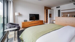 Ein modernes Hotelzimmer mit einem großen Bett, einem Fernseher, einer Holzkommode, einem Schreibtisch und einem Fenster mit Vorhängen.