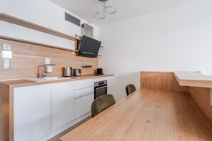 A modern kitchen with a wooden countertop, built-in appliances, and a dining area with a wooden table and chairs. - Blueground | Žižkov, view, nr Vítkov Park (PRG-93) (Prague)