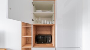 Eine Küche mit integriertem Mikrowellenherd, Holzregalen und weißen Schränken.