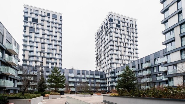Ein moderner Apartmentkomplex mit mehreren Hochhäusern, einem zentralen Innenhof mit Wasserspiel und umliegender Grünfläche.
