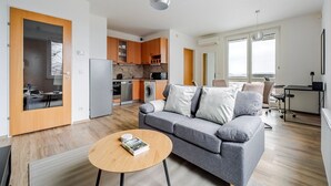 Eine moderne Wohnung mit grauem Sofa, Holzboden, einer Küche mit Holzausstattung, einem Essbereich und einem großen Fenster mit Blick.