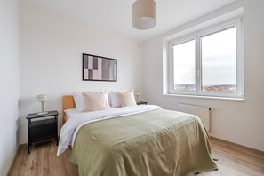 Une chambre à coucher comprenant un lit, une table de chevet, une lampe, une fenêtre donnant sur un paysage agréable et un radiateur.